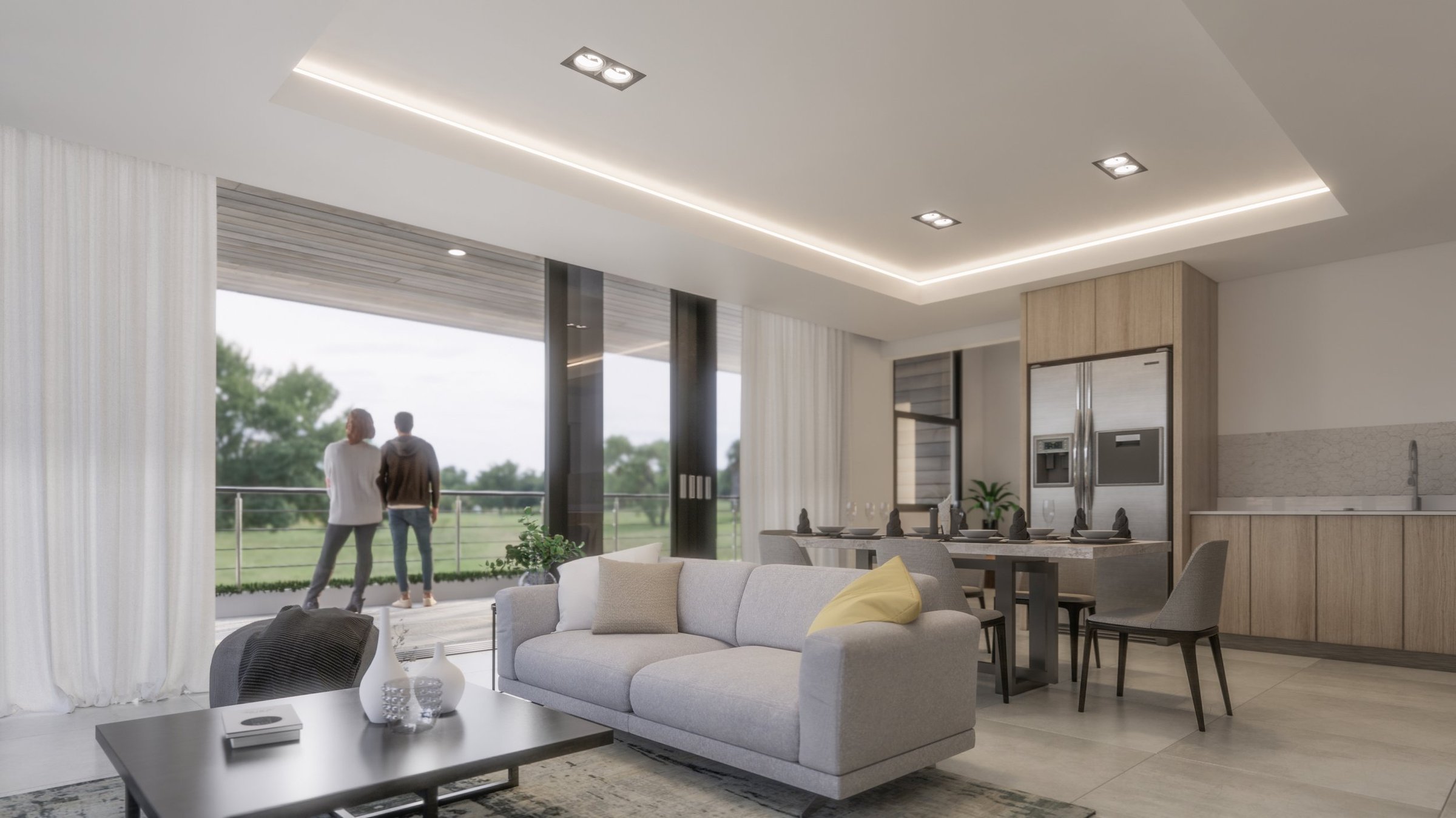 Modern living room with light-colored sofa, dining table, kitchen with stainless steel appliances, large windows showing outdoors with two people standing on the balcony.