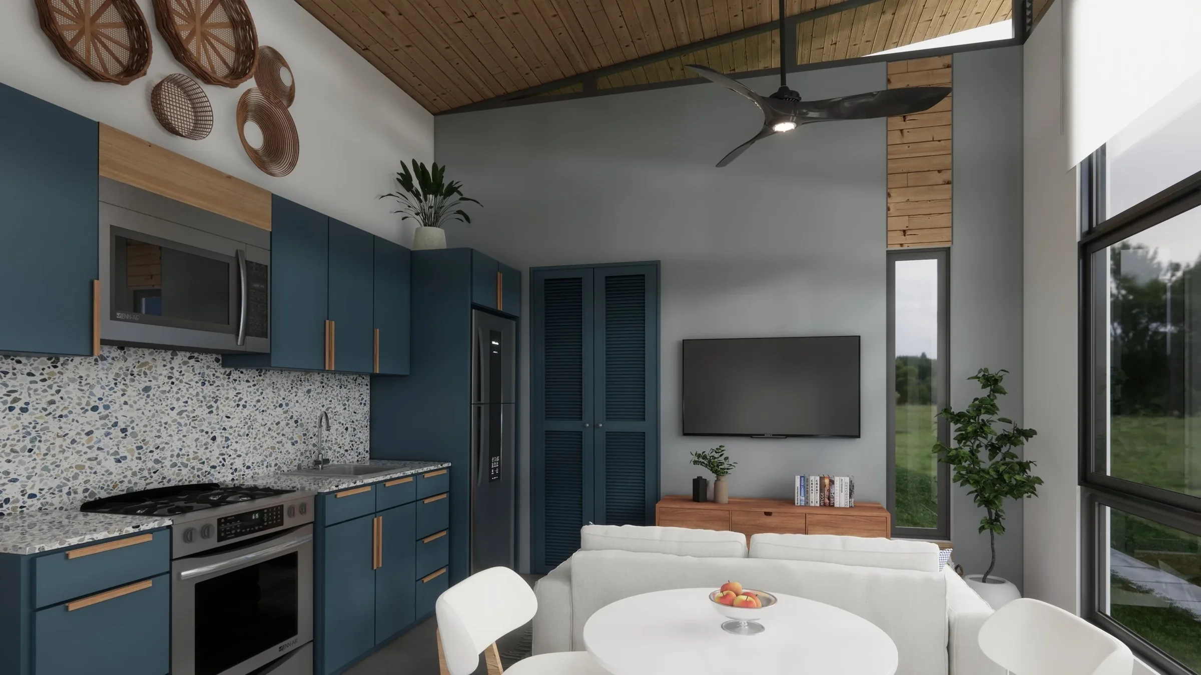 Modern living room with blue kitchen cabinets, a TV, and a white sofa. Large windows with a view of greenery outside, wooden ceiling and decor, including woven baskets on the wall, houseplants, and a dining table with a bowl of peaches.